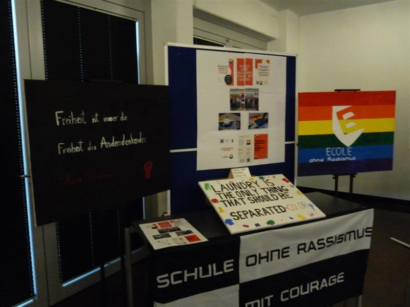  schwarze Tafel mit Aufschrift und Regenbogenflagge im Hintergrund in einem Raum anzeigen