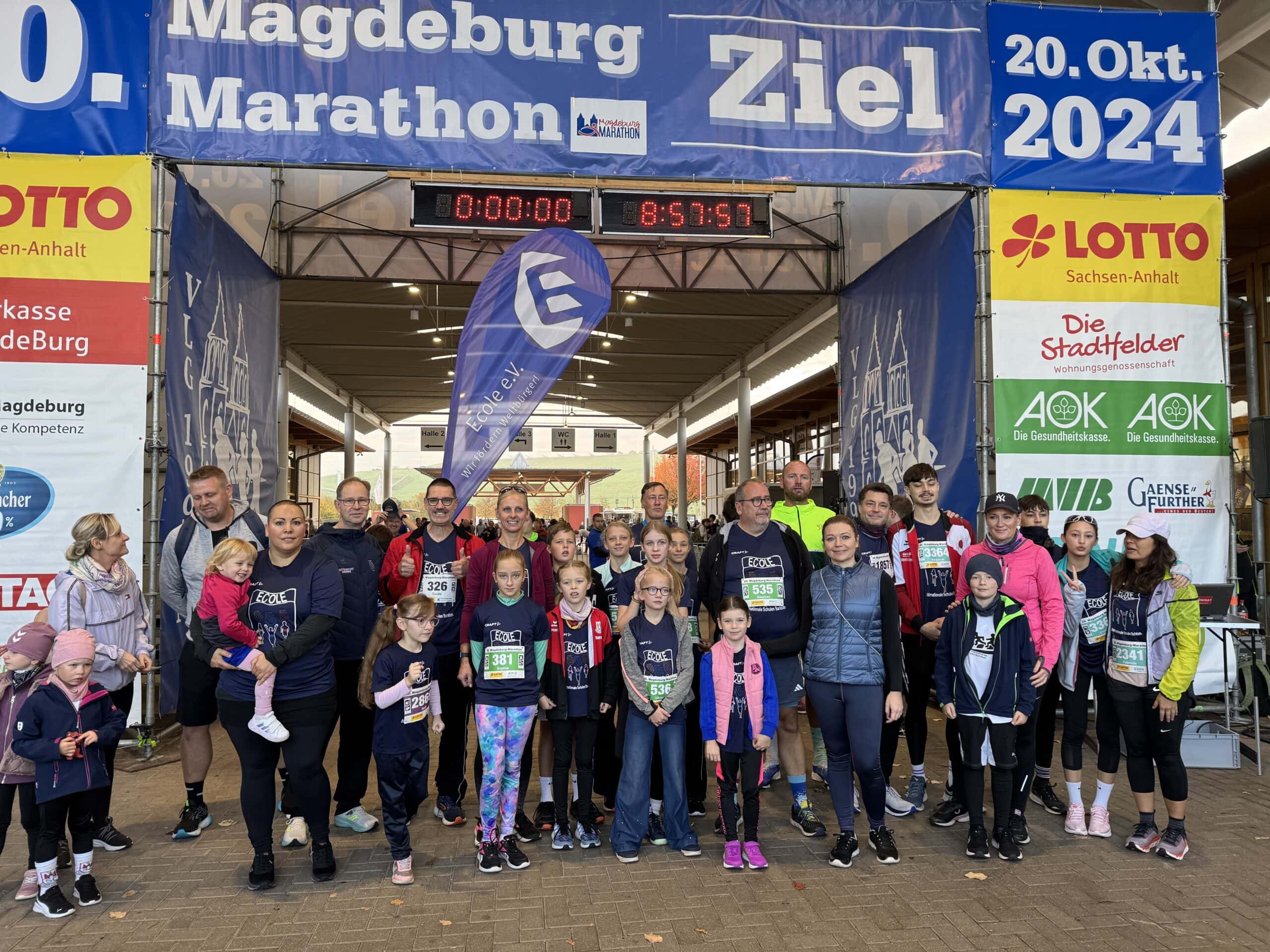 Gruppe von Menschen posiert lächelnd unter Marathon-Zielbanner, bunte Sportkleidung, Banner im Hintergrund.