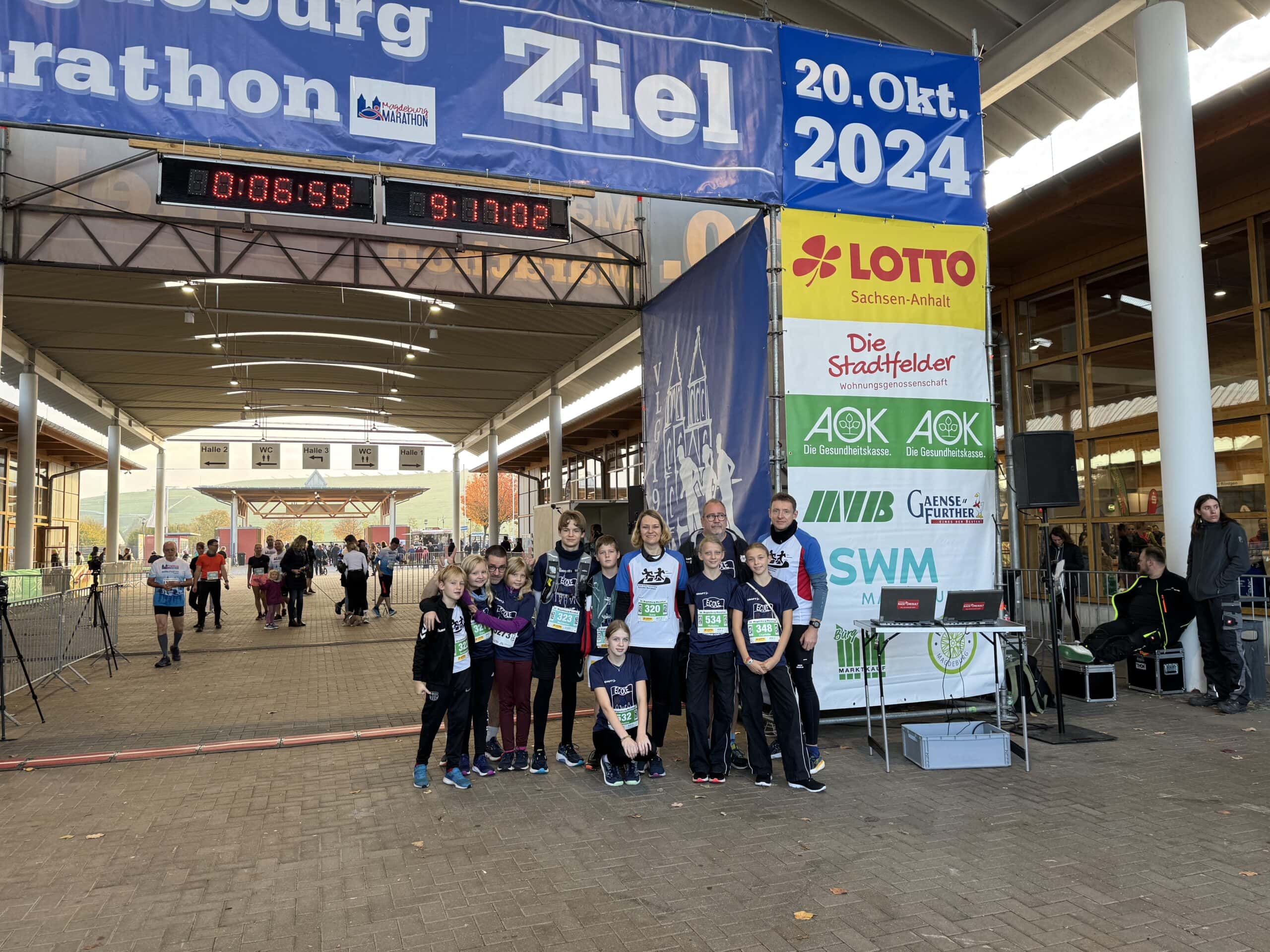 Menschen in Sportkleidung lächeln unter Marathon-Zielbanner in urbaner Umgebung. Farbenfroh gekleidet.