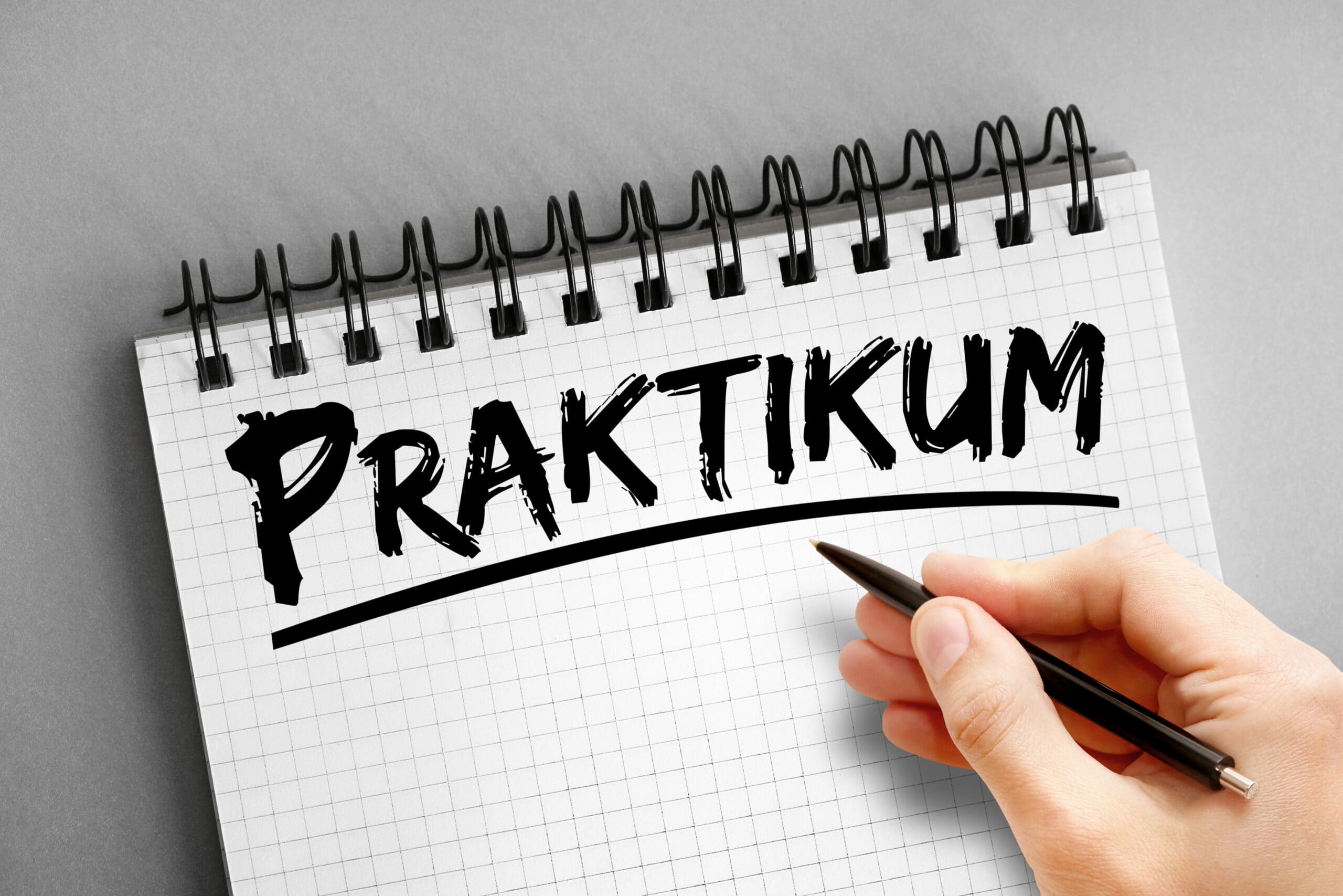 Notizblock mit dem handgeschriebenen Wort "Praktikum". Hand hält einen schwarzen Stift.