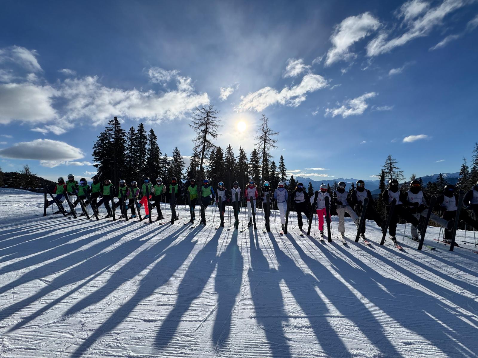 Gruppe von Skifahrern in grünen Westen bei Sonnenuntergang; lange Schatten auf schneebedecktem Boden.