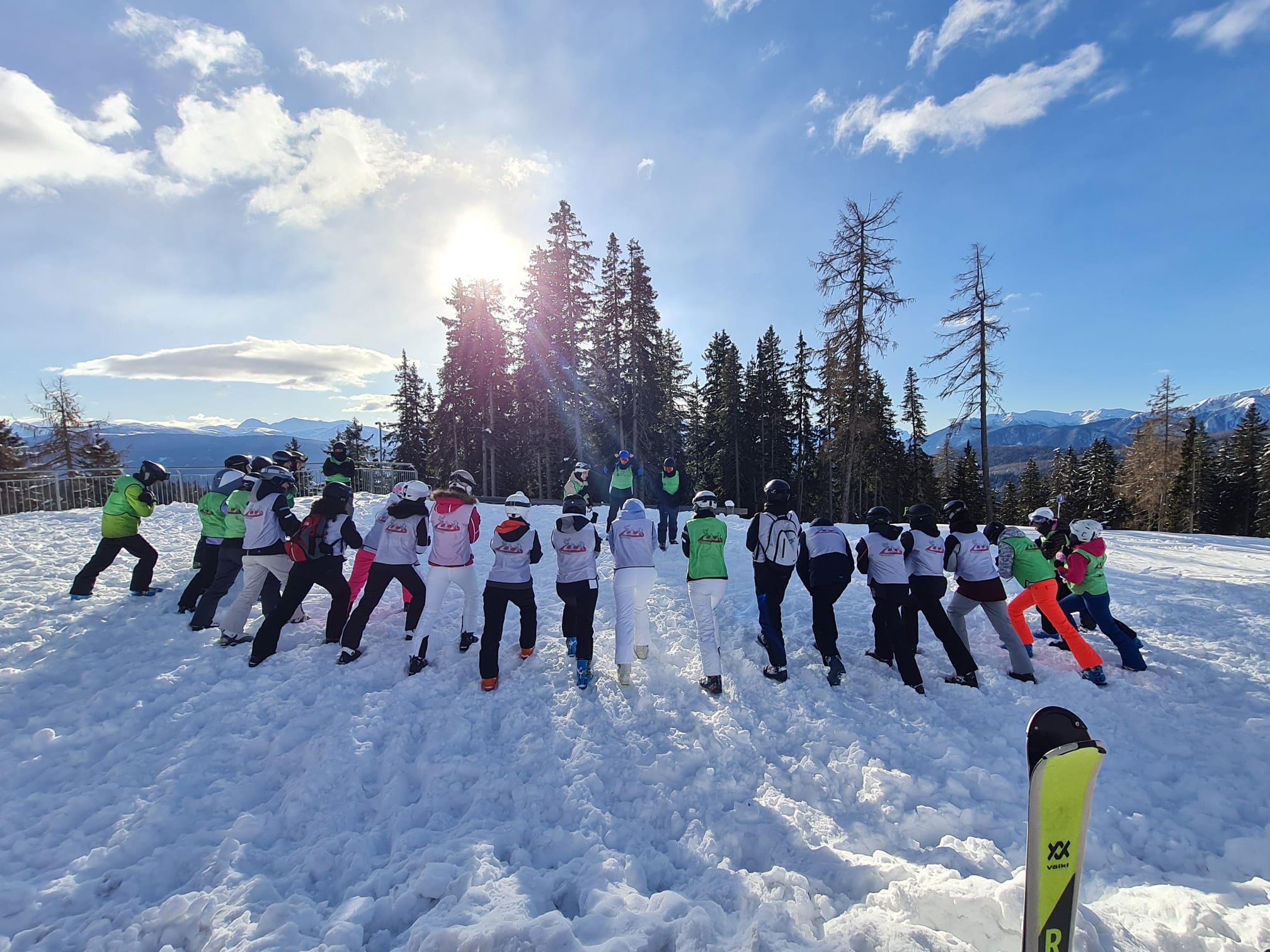 Eine Gruppe von Skifahrenden posiert fröhlich im Schnee vor sonniger Winterlandschaft.